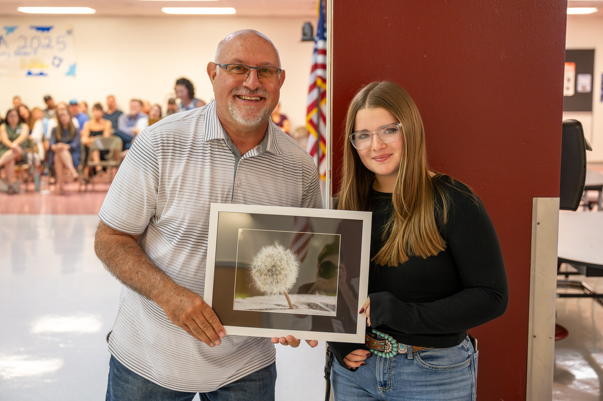 A board of education member standing proudly with a student, who gifted them artwork.